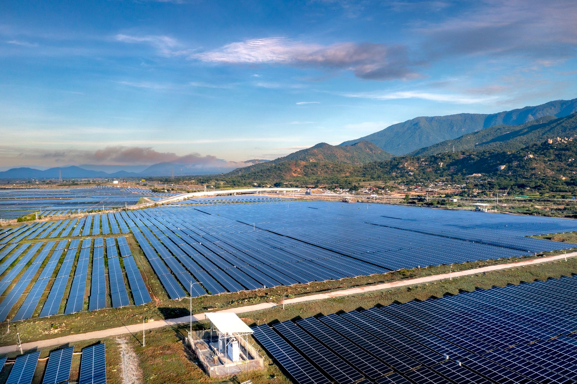 massive solar panel array under bright blue sky stretching across landscape mountains in distance golden sunlight reflecting off panels modern energy farm