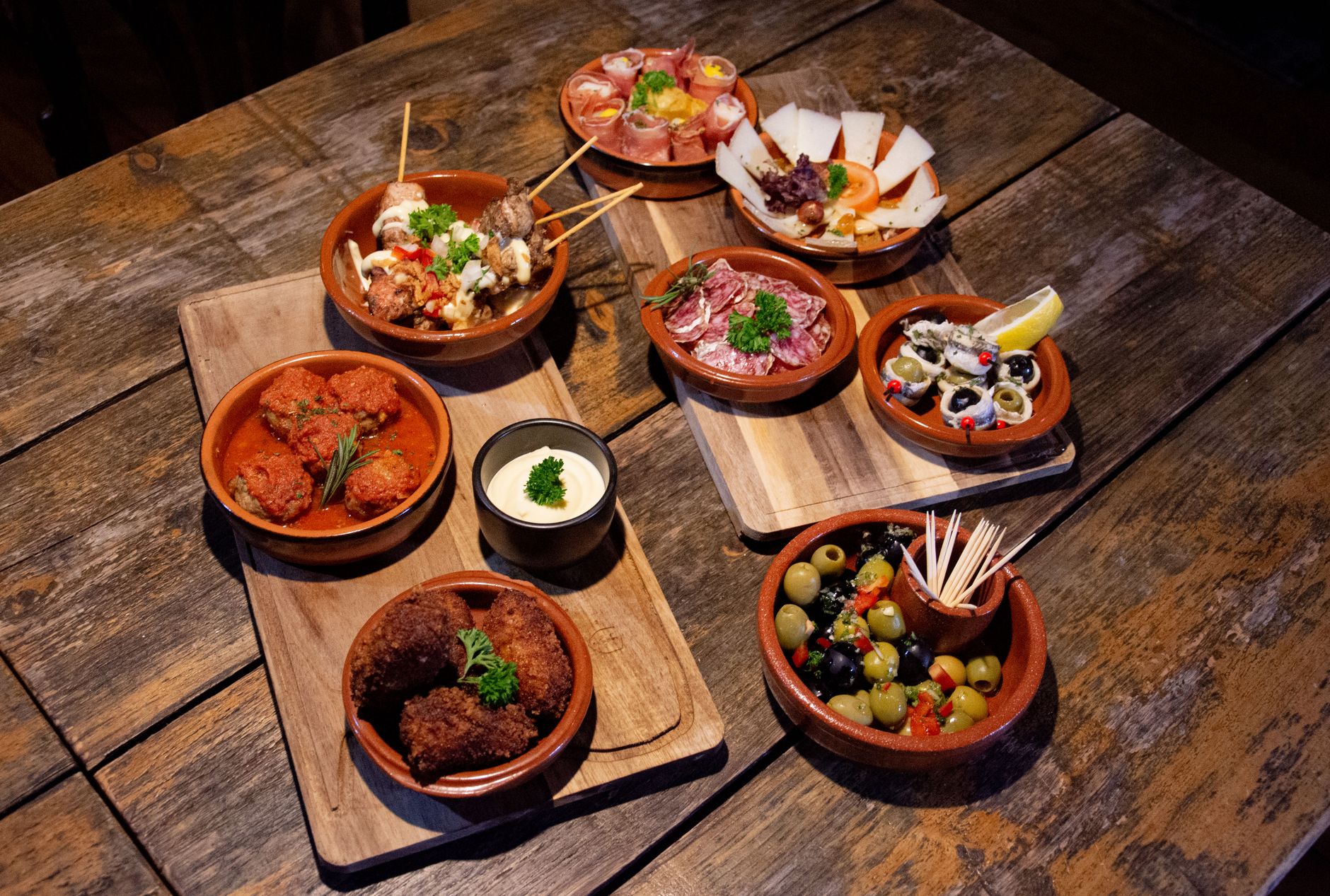 traditional spanish tapas variety on white plates, jamón, cheese, olives, bread, rustic wooden table, vibrant colors