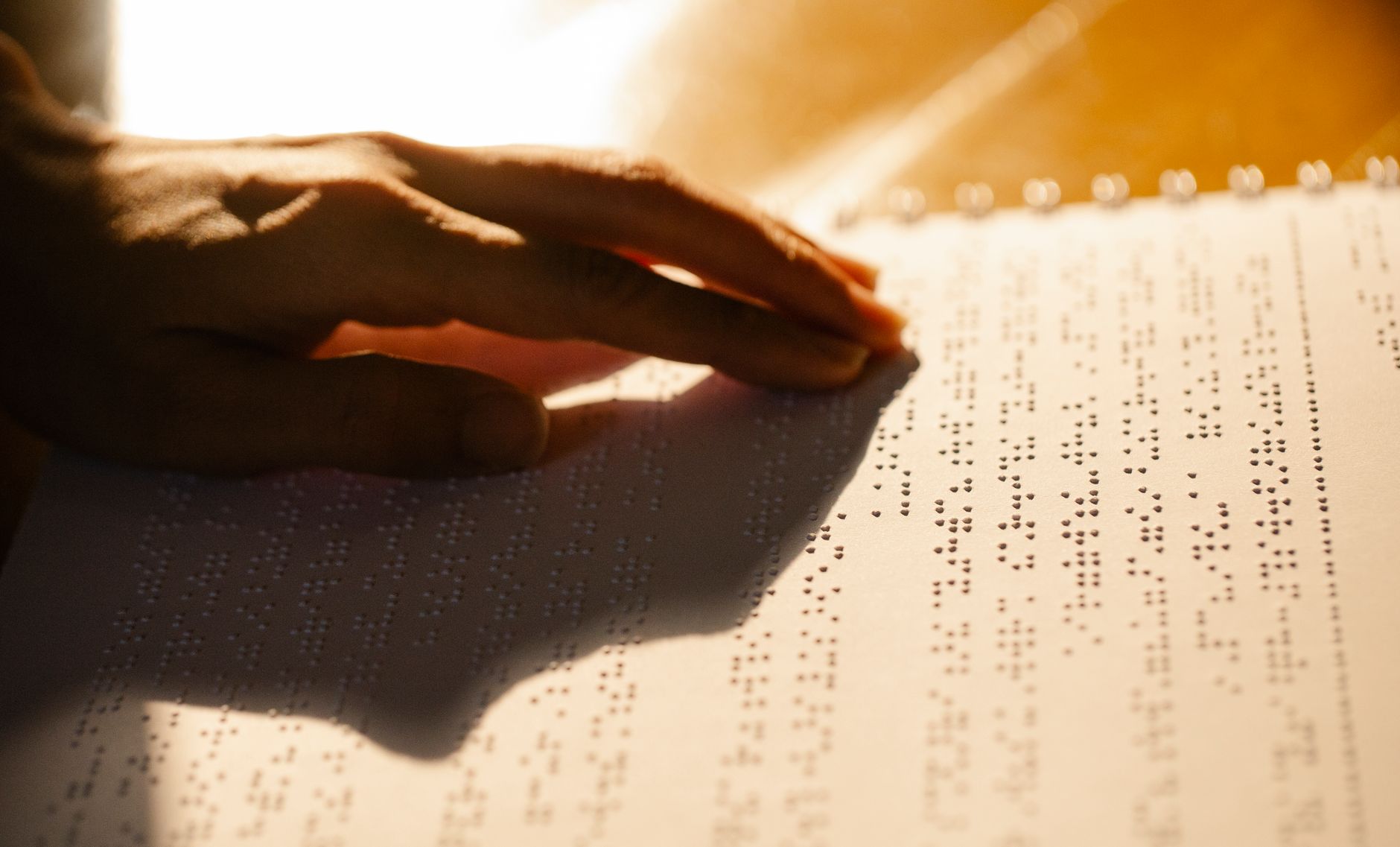 blind person reading braille book fingertips warm library light