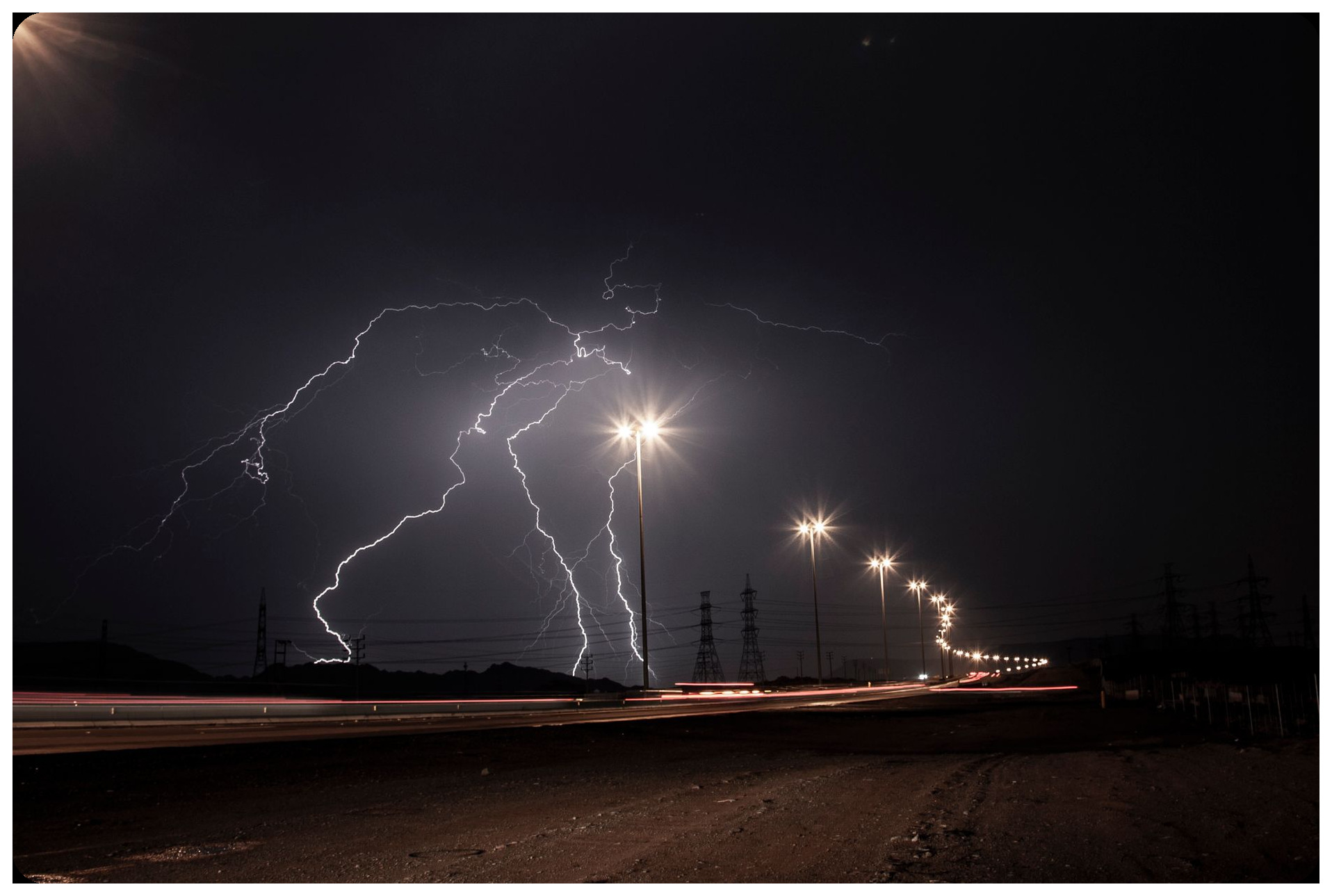 rainy night empty Spanish highway curving through landscape, street lights casting long shadows, dramatic weather and fog